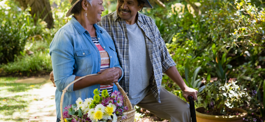 A senior couple hold a basket of flowers in a lush spring environment