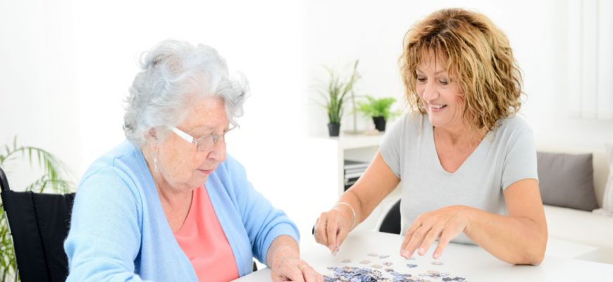 Middle aged woman doing puzzle with senior woman memory care for Alzheimer's